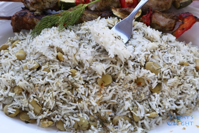 A platter of Persian rice with Lima beans, two sides of skewered beef and getting a bite using a fork.