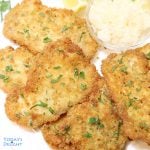 Pieces of pork schnitzel on a platter garnished with parsley and a side of lemon wedges and sauerkraut.