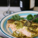 Salmon with lime, cilantro and jalapeno sauce on a plate with a piece of salmon on a fork and broccoli on the side. Wine glass and a bottle of wine in the background.