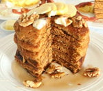 Sliced layers of Pumpkin Spice Pancake with syrup and topped with apple slices, walnuts.