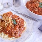 Pinoy style spaghetti with hot dog in meat sauce in a serving bowl and on a plate with a side of parmesan cheese.