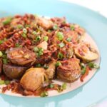 One serving of Brussel sprouts with bacon bits garnished with chopped green onions on a light blue plate.