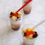 Three Asian desserts with mung beans, red beans, agar-agar, coconut milk, and shaved ice in plastic cups with red spoons.