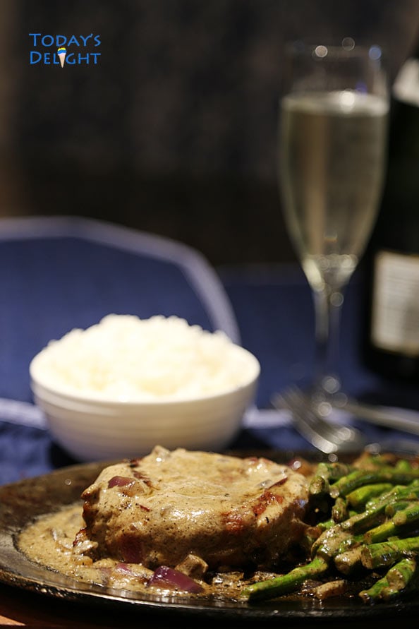 Rib Eye steak with side on a sizzling plate, a side of rice and a glass of wine.