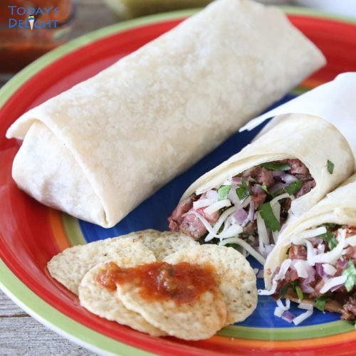 2 burritos with one cut in half and tortilla chips with red sauce.