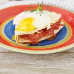 1 serving of ham, turkey, cheese sandwich wrap in tortilla with broken over easy egg yolk.