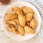 Patis fried chicken wings in a serving plate with sauce on the side.