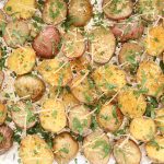 Oven Roasted Baby Potatoes garnished with cheese and parsley in baking sheet lined with foil.
