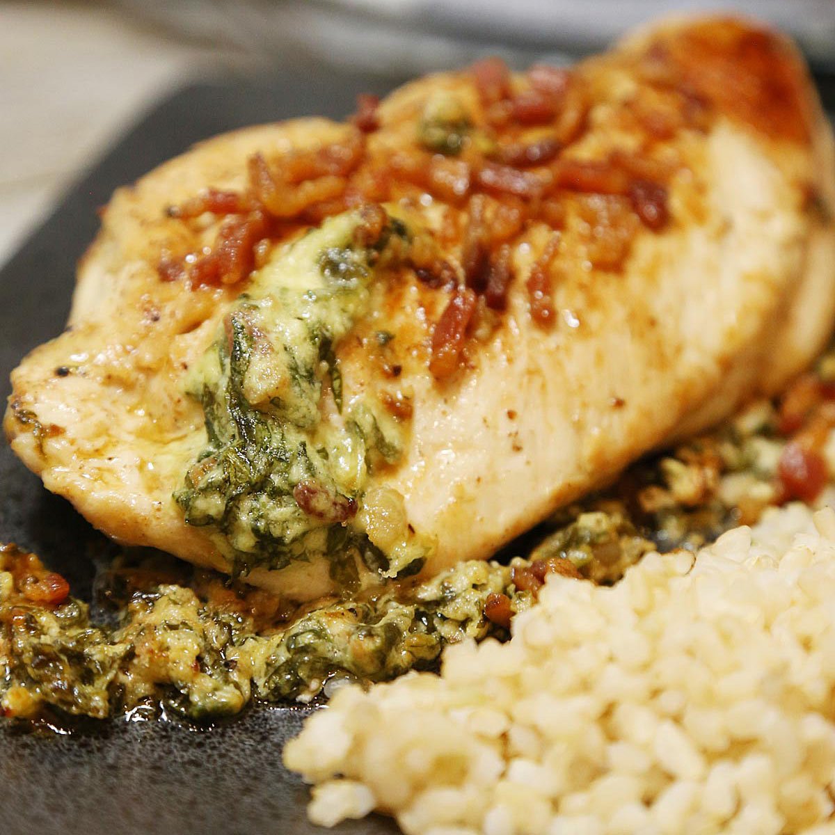 Plated spinach stuffed chicken breast garnished with bacon and a side of brown rice.