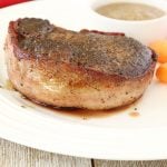Filet mignon steak wrapped in bacon with a side of mushroom sauce and baby carrots.