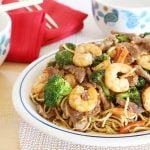 Pork, vegetable, shrimp lo mein in a serving platter with 2 bowls, red napkins and chop sticks on the side.
