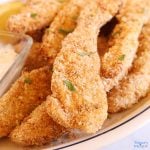 Air fried chicken tenders on a platter garnished with fresh parsley flakes, a side of lemon wedges and sauce.