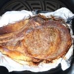 One cooked bone-in ribeye steak lined with foil in air fryer basket.