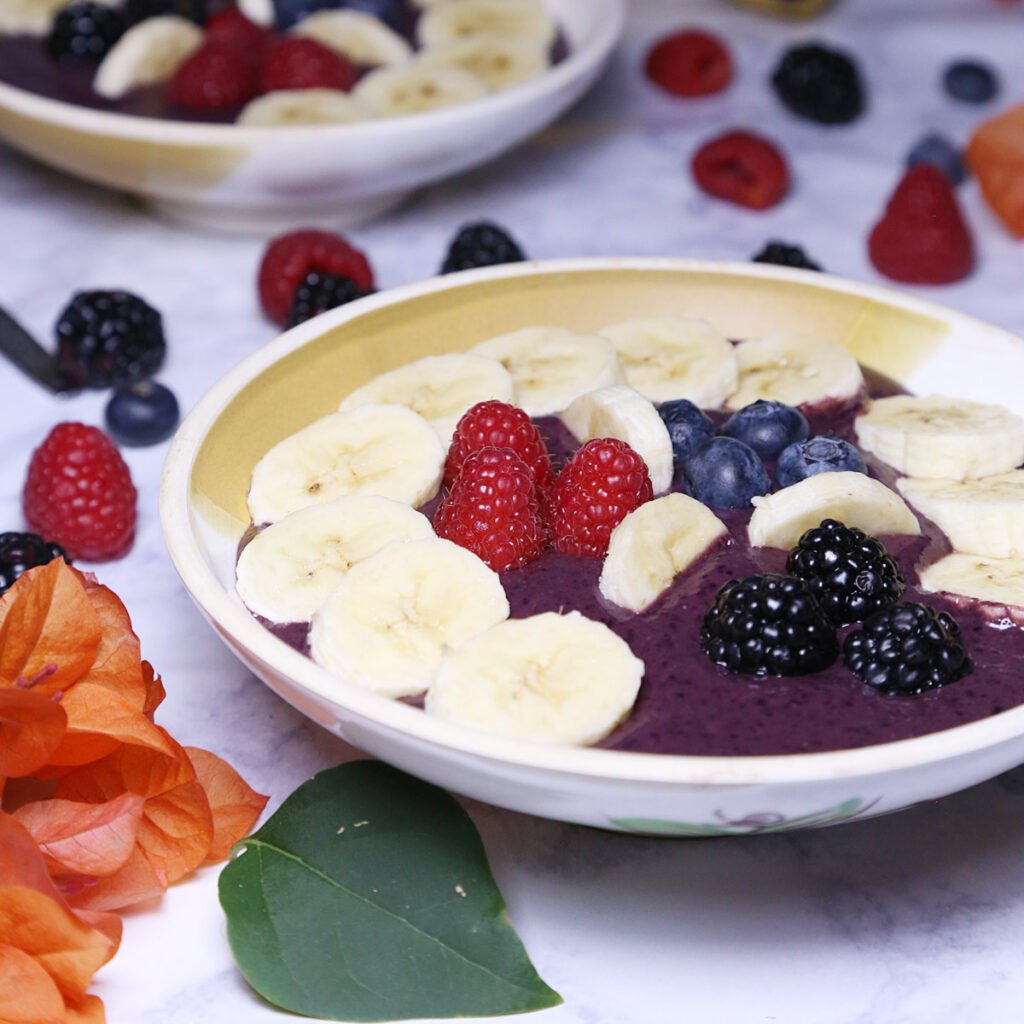 Two creamy acai bowls with pieces of blackberries, blueberries, raspberries and sliced bananas.