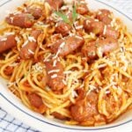 Spaghetti with whole little smokies sausages garnished with grated cheese and chopped parsley on a platter.